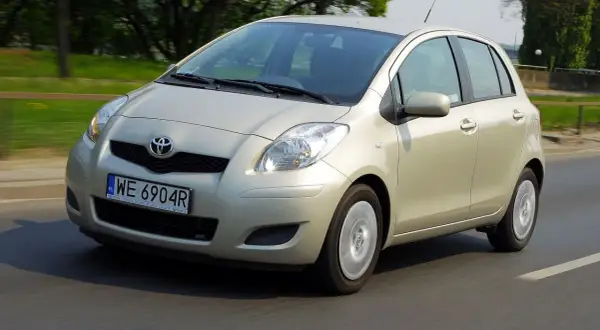 Złoty Toyota Yaris 2006 na drodze, z zielenią w tle.