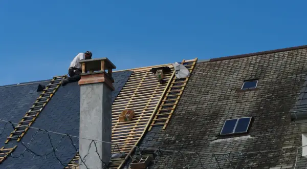 Un couvreur travaille sur un toit en ardoise, en cours de rénovation. Ces gros travaux pourraient ouvrir droit à une déduction fiscale pour le nu-propriétaire.