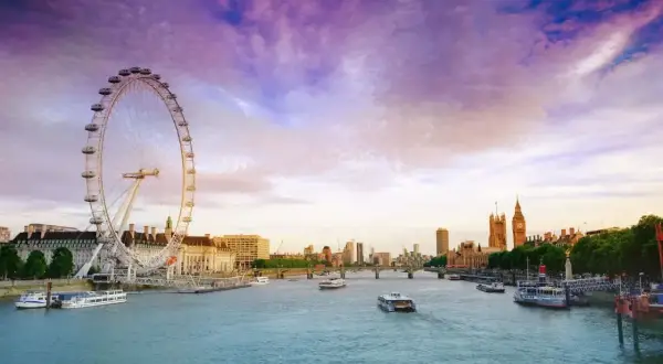 Zachód słońca nad Tamizą, z widokiem na London Eye i Parlament. Rzeka w Londynie lśni w purpurowym niebie.