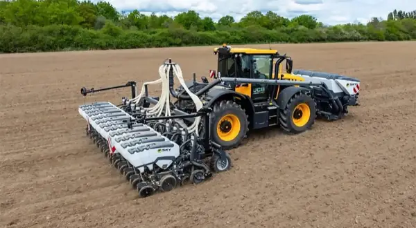 Żółty traktor z przyczepionym nowoczesnym siewnikiem do nawozu ogrodowego pracuje na pustym polu.