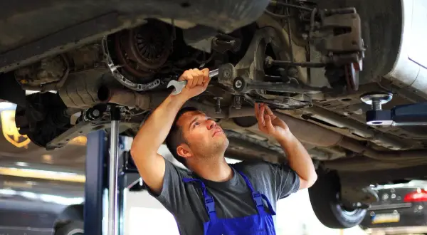Mechanik dokonuje wymiany tulei wahacza, pracując pod podniesionym samochodem.