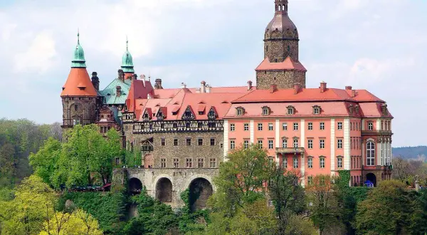 Imponujące zamki w okolicy Wrocławia, z wieżami i czerwonymi dachami, otoczone zielenią.