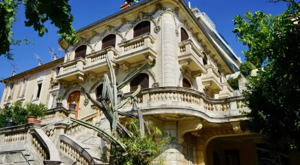 Élégante villa abandonnée sur la Côte d'Azur, avec un grand escalier en pierre et un cactus imposant devant sa façade ornée.
