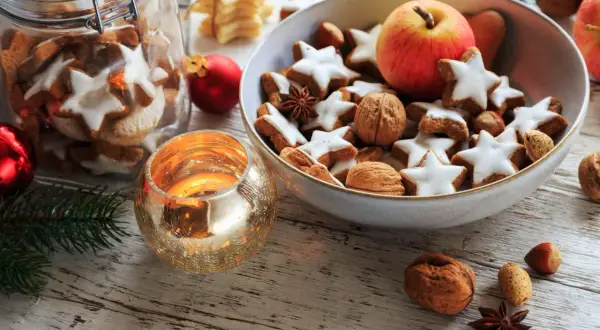 Weihnachtsplätzchen, Nüsse und ein Apfel in einer Schale, dazu eine Kerze – das ist die Bedeutung von Weihnachten: Gemütlichkeit und Genuss.