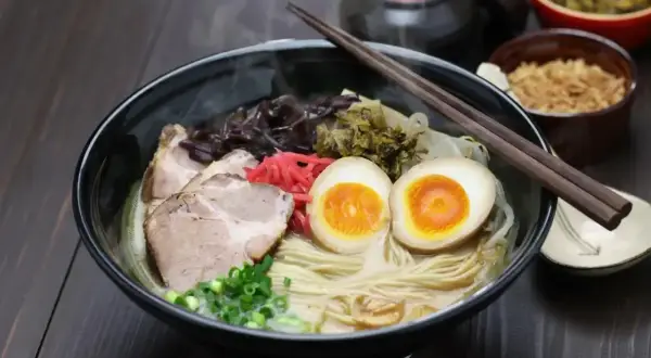 Pyszny ramen: makaron, plastry wieprzowiny, jajko na pół, szczypiorek i marynowane warzywa. Idealny na rozgrzewkę.