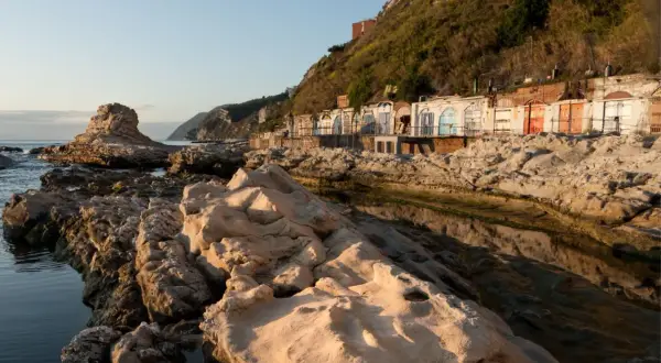 Scogliere rocciose e cabine colorate sulla spiaggia del Passetto, illuminate dalla luce dorata del tramonto.