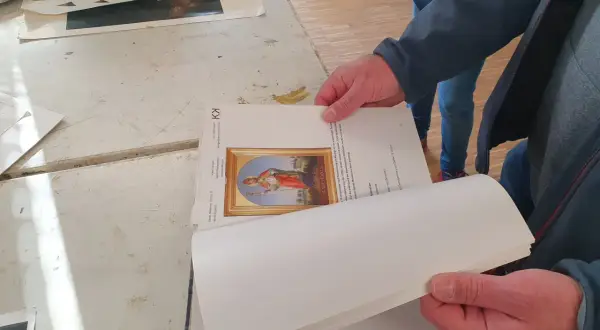 Hände halten ein Buch mit einem Bild eines Heiligen. Ein Detail der Kunstrestauration.