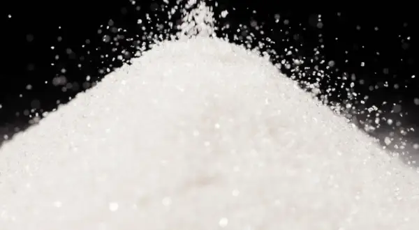 Biały, drobny proszek, przypominający cukier lub sorbitol, sypie się na stożek.