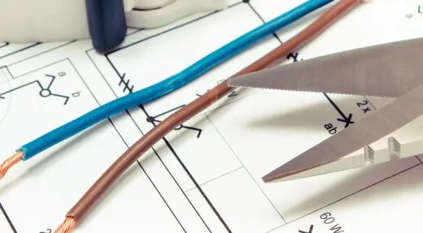 Niebieski i brązowy kabel, gotowe do cięcia, leżą na schemacie elektrycznym.