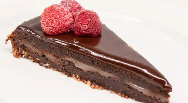 En bit kladdkaka med After Eight-smak, toppad med tre hallon på en vit tallrik.