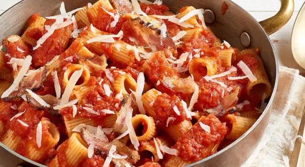 Rigatoni all'amatriciana dans une poêle en cuivre, garni de copeaux de parmesan. Un plat réconfortant et savoureux.