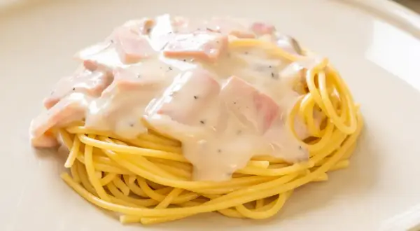Pyszny makaron z serem i kawałkami szynki w kremowym sosie.