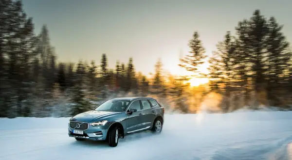 Volvo XC60 med d4 motor kör på snöig väg i solnedgången.