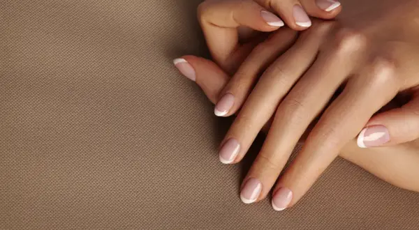 Dłonie z idealnym frenczem, podkreślającym naturalne kolory paznokci. Delikatny manicure na beżowym tle.