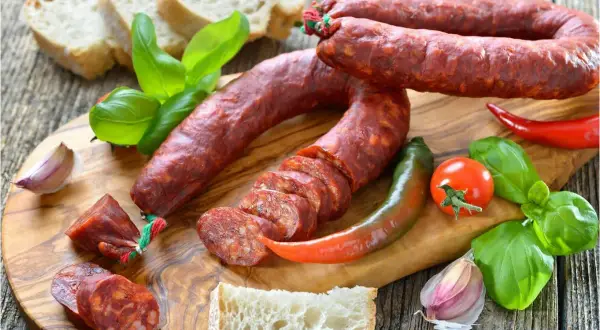 Chorizo co to? Pikantna kiełbasa, chleb, papryczki, pomidor i bazylia na desce.