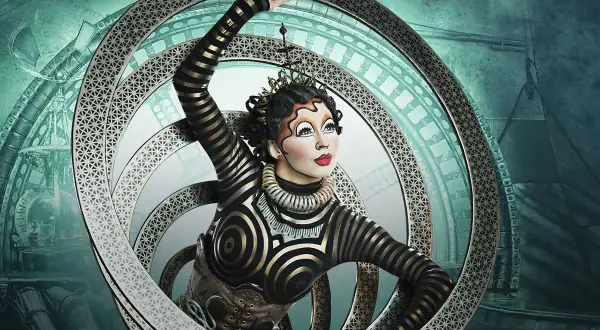 Artista del circo del sol en Zaragoza, con un traje de rayas doradas y negras, dentro de un aro metálico con intrincados diseños.