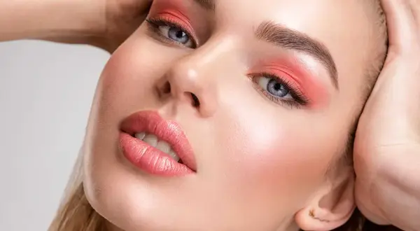 Viso di donna con ombretto corallo e un delicato blush o fard sulle guance.