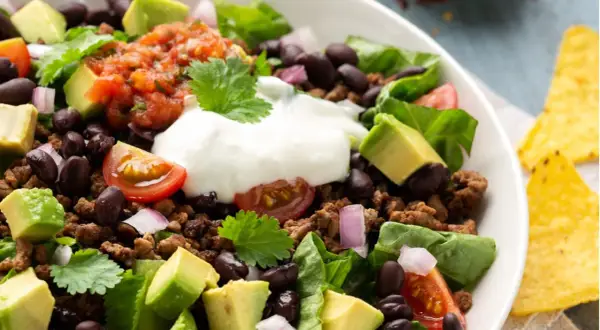 Ein bunter Taco Salat mit Hackfleisch, schwarzen Bohnen, Avocado, Tomaten, Zwiebeln und einem Klecks Sauerrahm. Perfekt für einen leichten Genuss.