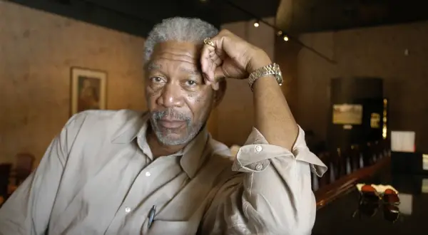 Morgan Freeman młody, z siwą brodą i zmarszczkami, opiera głowę na dłoni.