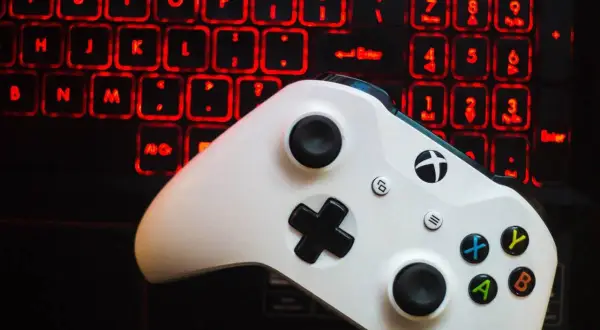 Biały kontroler Xbox One na tle podświetlanej na czerwono klawiatury.