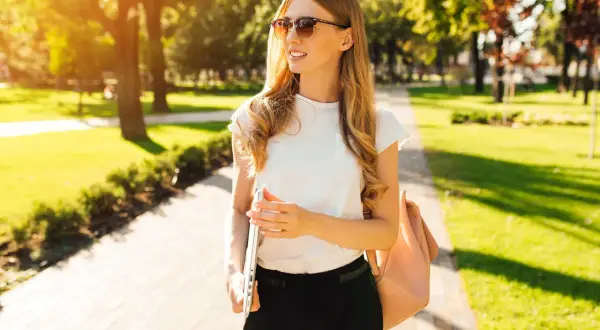 Junge Frau im **summer business casual** Look, mit Laptop und Tasche, genießt die Sonne im Park.