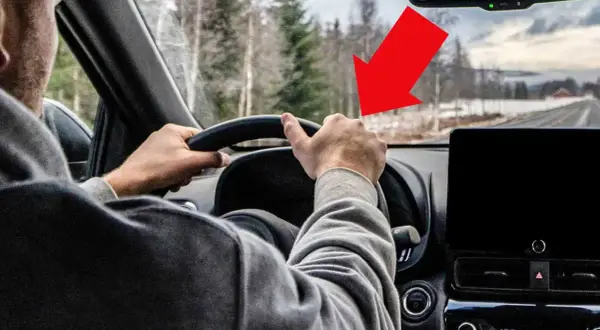 Förarens händer på ratten, en röd pil pekar mot vägen där det kan finnas vibrationer i bilen.