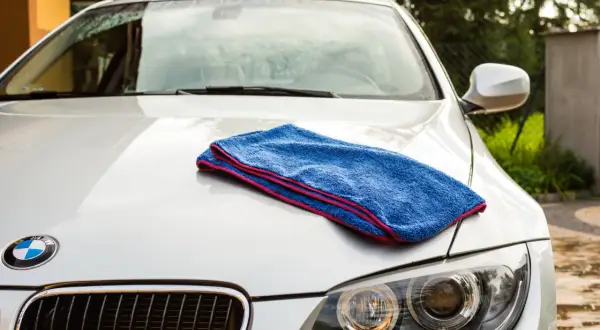 Niebieski ręcznik do osuszania auta leży na masce białego BMW. Idealny do rankingu najlepszych akcesoriów do pielęgnacji samochodu.