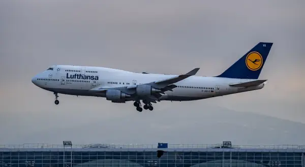 Lufthansa Boeing 747 im Landeanflug über einem modernen Flughafengebäude.
