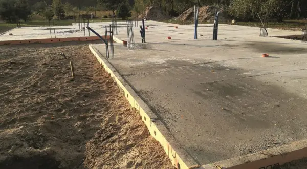 Płyta fundamentowa w budowie, widać zbrojenie i rury. Trudno ocenić, ile betonu na płytę fundamentową potrzeba bez dokładnych wymiarów.