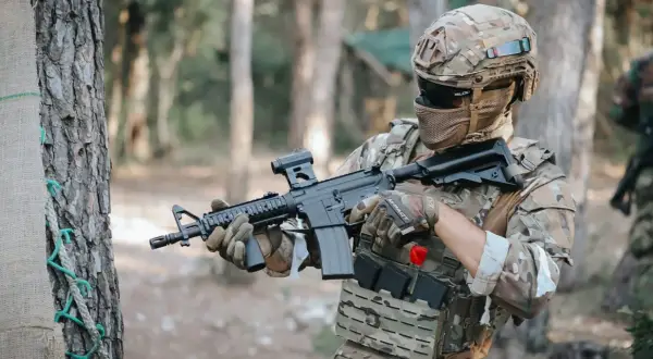 Jugador de fps airsoft con casco y rifle táctico, listo para la acción en un bosque.