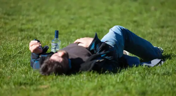 Mężczyzna leży na trawie obok butelki alkoholu, być może doświadczając skutków ubocznych po narkotykach, takich jak drgawki.