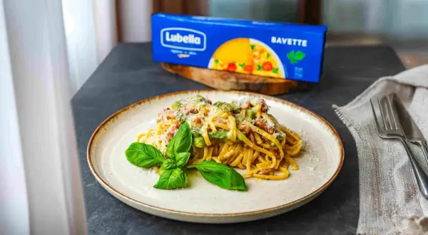 Pyszna carbonara ze szparagami na talerzu, udekorowana bazylią. Obok opakowanie makaronu Lubella Bavette.