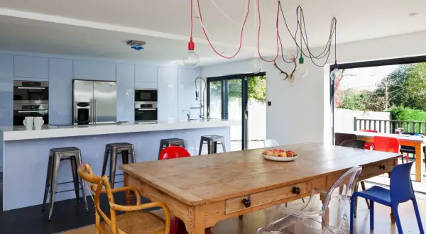 Un affascinante abbinamento sedie Kartell con tavolo antico in legno, circondato da una cucina moderna e un giardino lussureggiante.