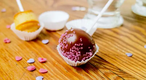 Schokoladen-Cake-Pops mit rosa Zuckerstreuseln und ein ungefüllter Cake Pop, bereit für ein einfaches cake pops rezept.