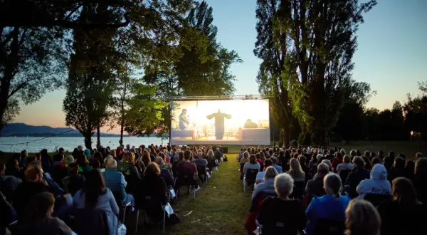 Open-air Kino in Boxberg: Viele Menschen sitzen auf Stühlen und schauen einen Film auf einer großen Leinwand am Seeufer.