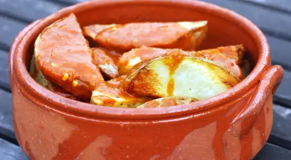 Patatas bravas, pommes de terre croustillantes nappées d'une sauce épicée, servies dans un plat en terre cuite.
