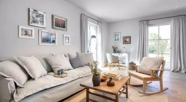 Gemütliches wohnzimmer grau blau holz mit großem Sofa, Holztisch und Schaukelstuhl. Bilder an der Wand und Fenster mit Vorhängen.