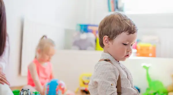 Chłopiec w koszuli z szelkami bawi się zabawkami. Kiedy można oddać dziecko do żłobka? Wesołe dzieciństwo.