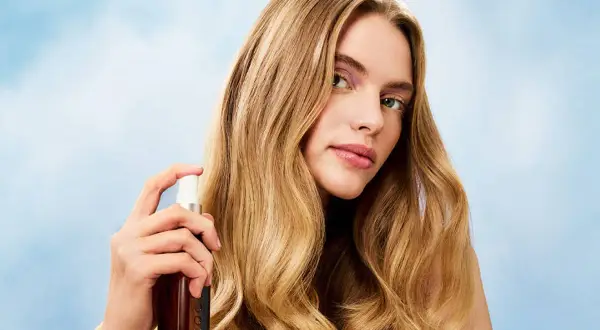 Mujer rubia aplica bruma en su pelo, logrando un brillo radiante.