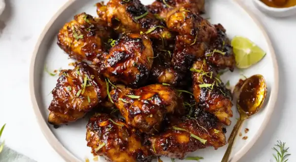 Krispiga kycklingvingar med en glansig glaze, garnerade med lime och örter. Ett perfekt recept för en smakrik glaze!