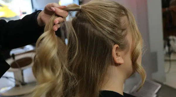Tworzenie fryzury na Dzień Kobiet. Dłoń modeluje blond włosy, przygotowując je do stylizacji.
