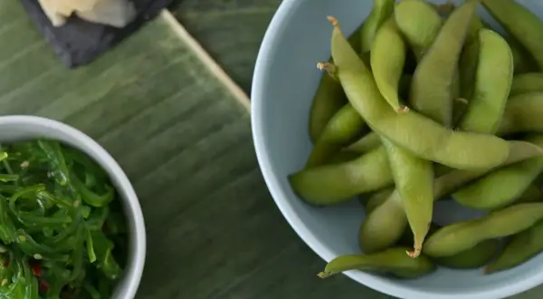Miseczka z zieloną fasolką edamame, obok sałatka z wodorostów i plasterki imbiru na liściu bananowca.