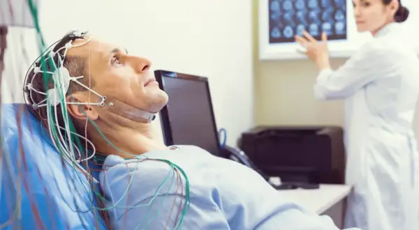 Mężczyzna leży z elektrodami na głowie do badania eeg. Lekarka analizuje wyniki na ekranie.