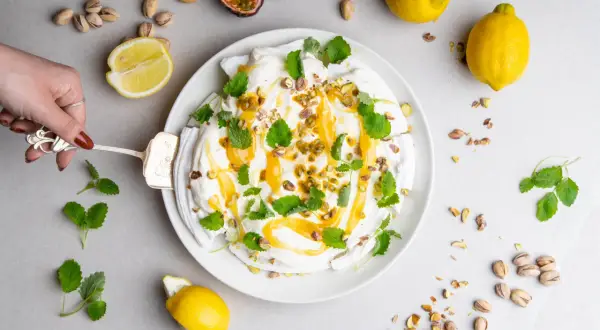 En vacker pavlova med lemoncurd, toppad med pistagenötter och mynta. Serveras med färska citroner och passionsfrukt.
