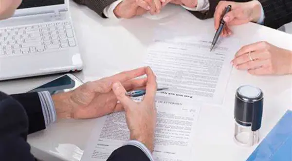 Manos revisando documentos, uno de ellos es un **hipotecante no deudor**, junto a un sello y portátil.