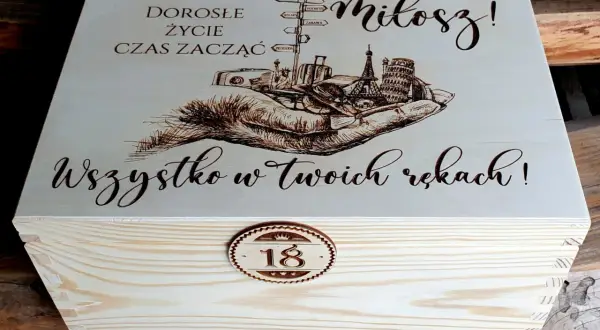 Drewniana skrzynka z grawerem: dłonie, walizki, wieże, drogowskazy, napis "Miłosz!" i "Wszystko w Twoich rękach!".