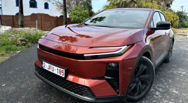 Nowa Toyota w kolorze miedzianym, zaparkowana przed białym budynkiem z niebieskimi oknami.