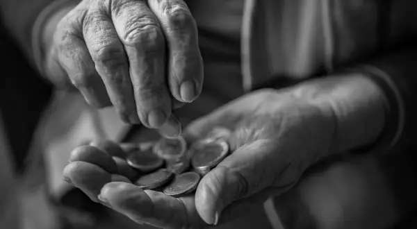 Mani anziane contano monete, un gesto che evoca la domanda su a quanto ammonta l'assegno di accompagnamento.