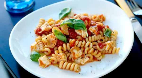 En tallrik med spiralformad pasta, tomat och bitar av mozzarella, toppad med färsk basilika. En härlig pasta med mozzarella.