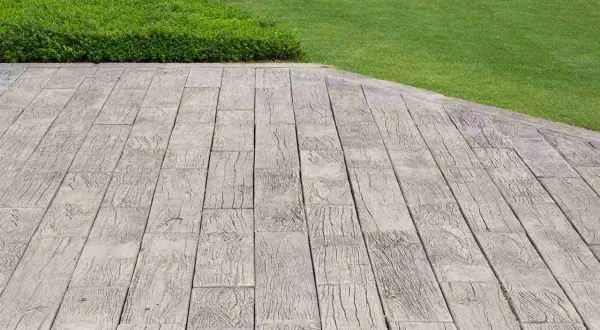 Pavimentazione marciapiede in cemento stampato effetto legno, adiacente a un prato verde ben curato.